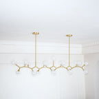 Unlit Clérachic chandelier with clear globes along a gold frame, hung from two rods in a corner with a white cornice.