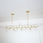 Angled view of the unlit Clérachic chandelier, its clear globes and gold branches hung from two rods of different lengths.