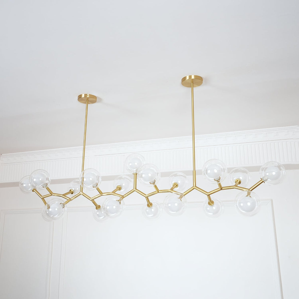 Angled view of the unlit Clérachic chandelier, its clear globes and gold branches hung from two rods of different lengths.