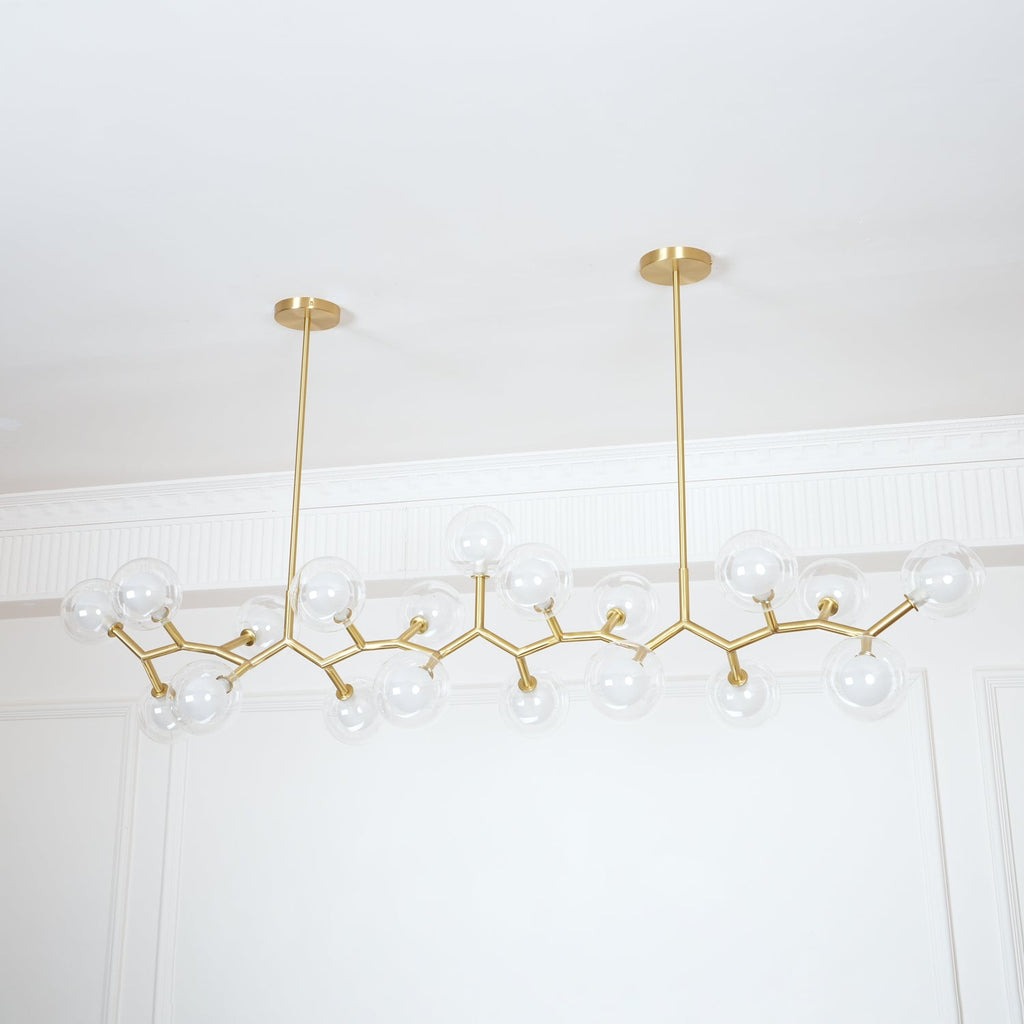 Clérachic chandelier with clear glass globes along its gold branches, unlit, below a white ceiling with a decorative cornice.