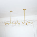 Clérachic chandelier with clear glass globes along its gold branches, unlit, below a white ceiling with a decorative cornice.