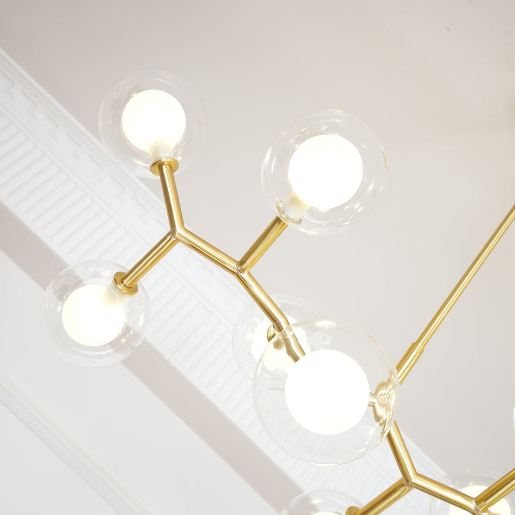 Close view from below of glowing globes and the angled gold branches of this Clérachic chandelier, beside white ceiling moulding.
