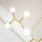 Close view from below of glowing globes and the angled gold branches of this Clérachic chandelier, beside white ceiling moulding.
