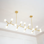 Lit Clérachic chandelier hung from two gold rods, with glowing globes spread along zigzag gold branches under a moulded ceiling.