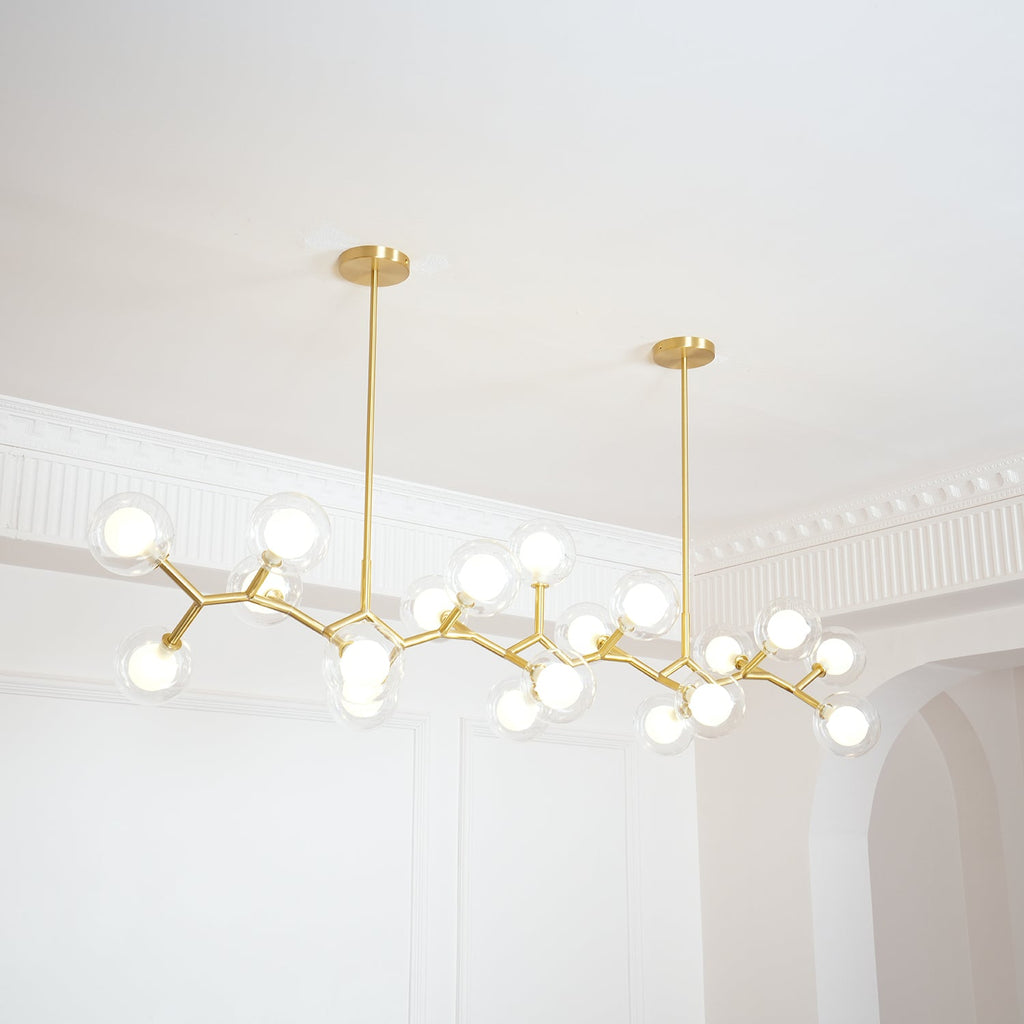 Clérachic chandelier lit with its globes on gold branches, seen at an angle beside an arched doorway and white ceiling moulding.