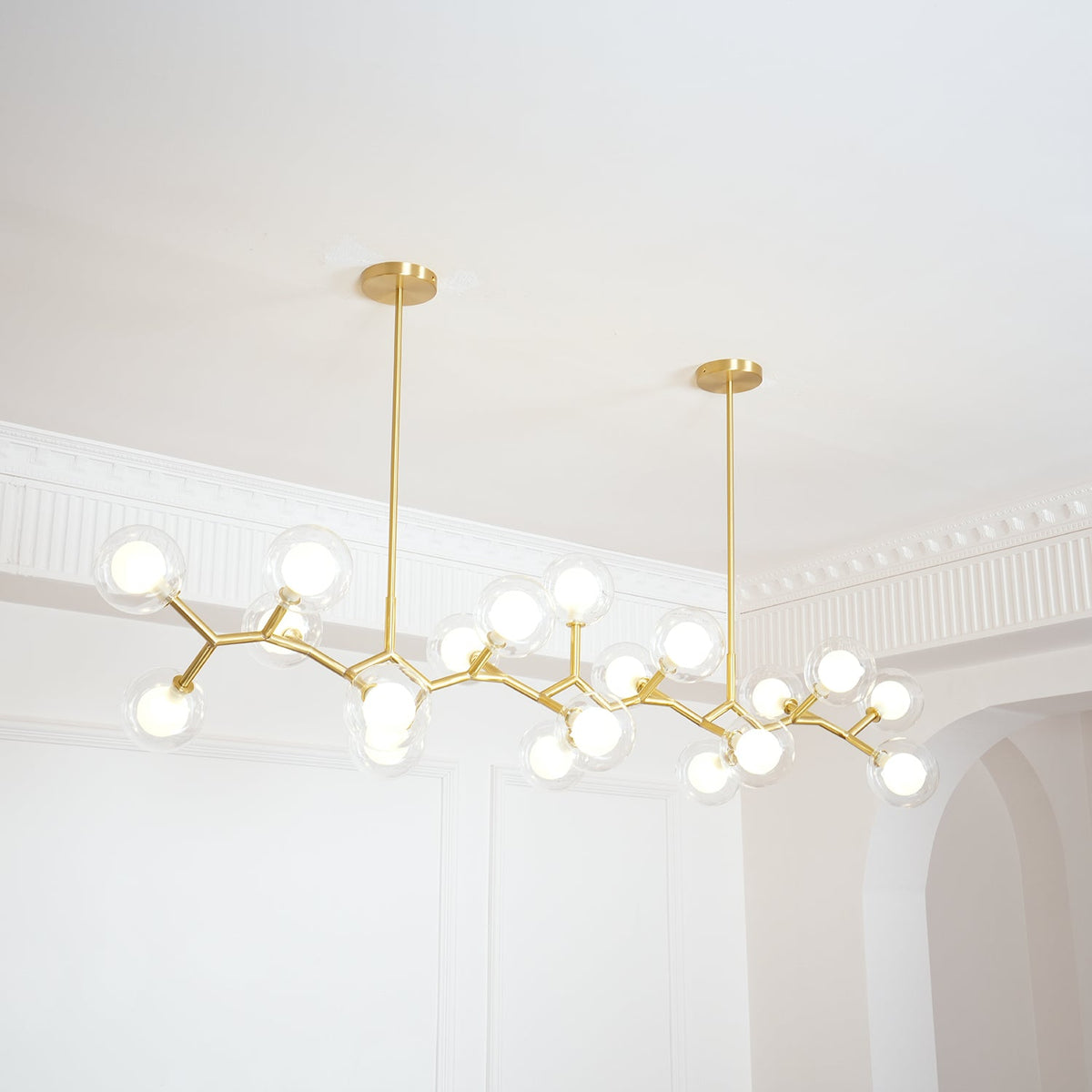 Clérachic chandelier lit with its globes on gold branches, seen at an angle beside an arched doorway and white ceiling moulding.