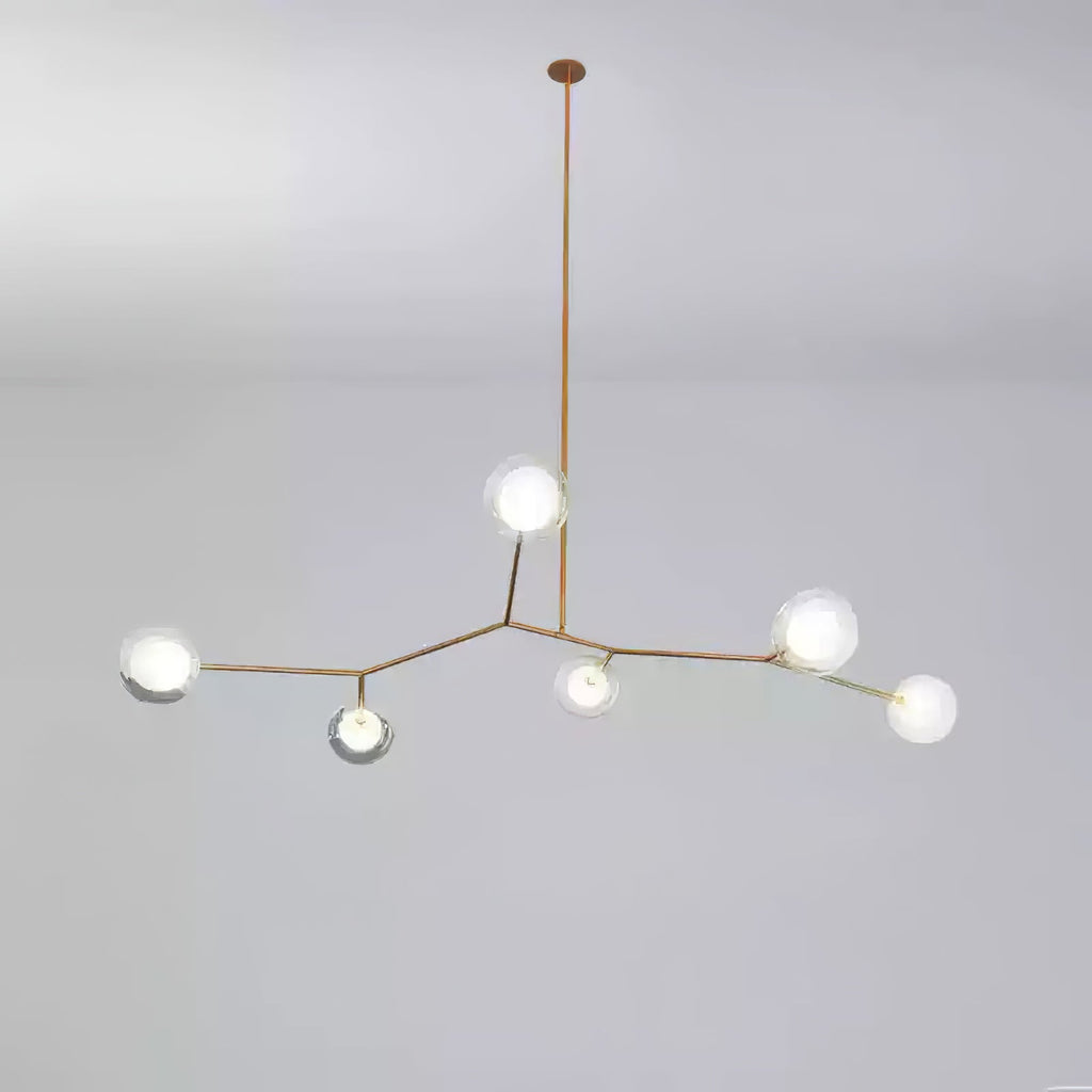 Small Clérachic gold-branch chandelier with six glass globes lit, hung from one long rod against a soft grey backdrop.