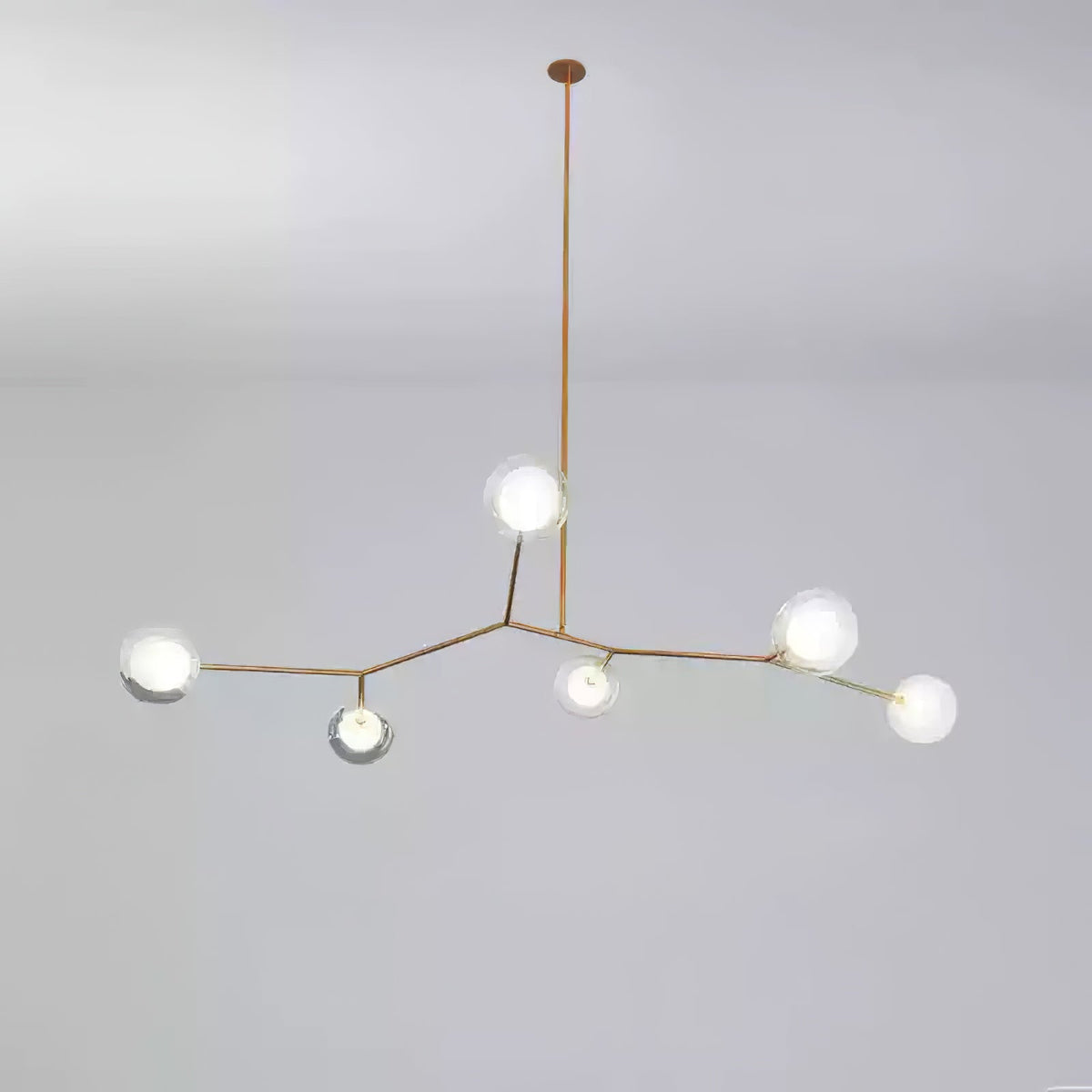 Small Clérachic gold-branch chandelier with six glass globes lit, hung from one long rod against a soft grey backdrop.