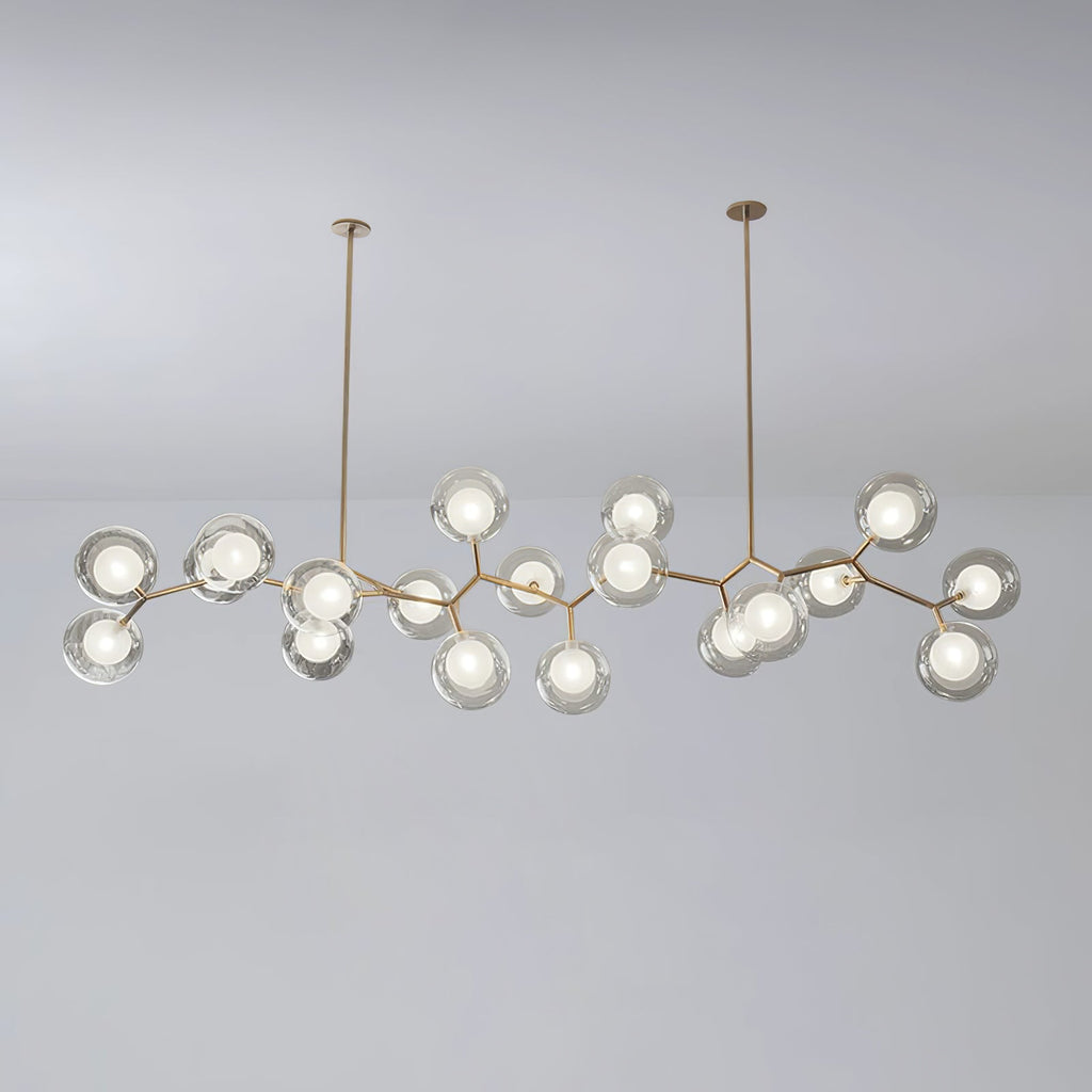Large Clérachic chandelier with many lit glass globes on gold branches, hung from two rods against a soft grey backdrop.