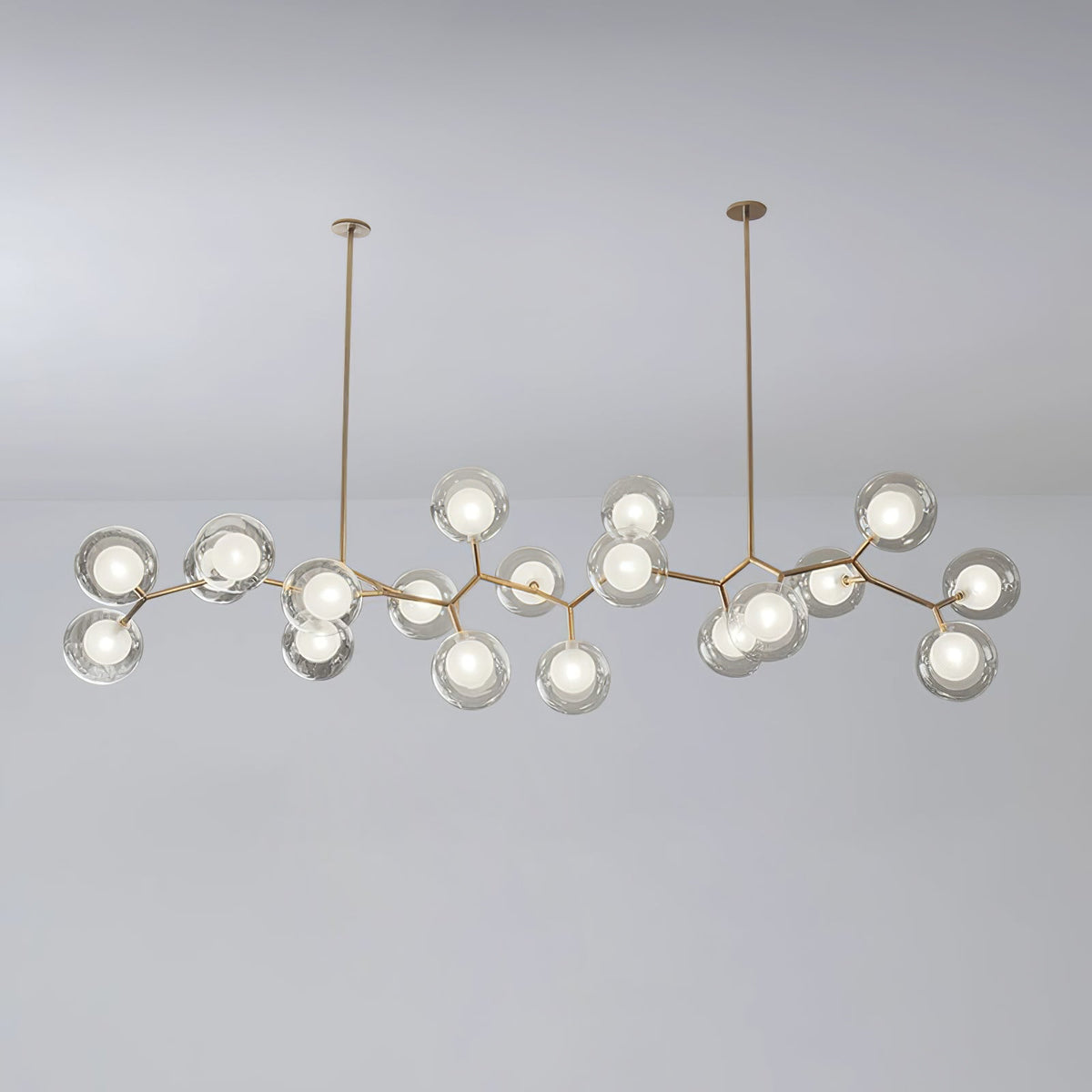 Large Clérachic chandelier with many lit glass globes on gold branches, hung from two rods against a soft grey backdrop.