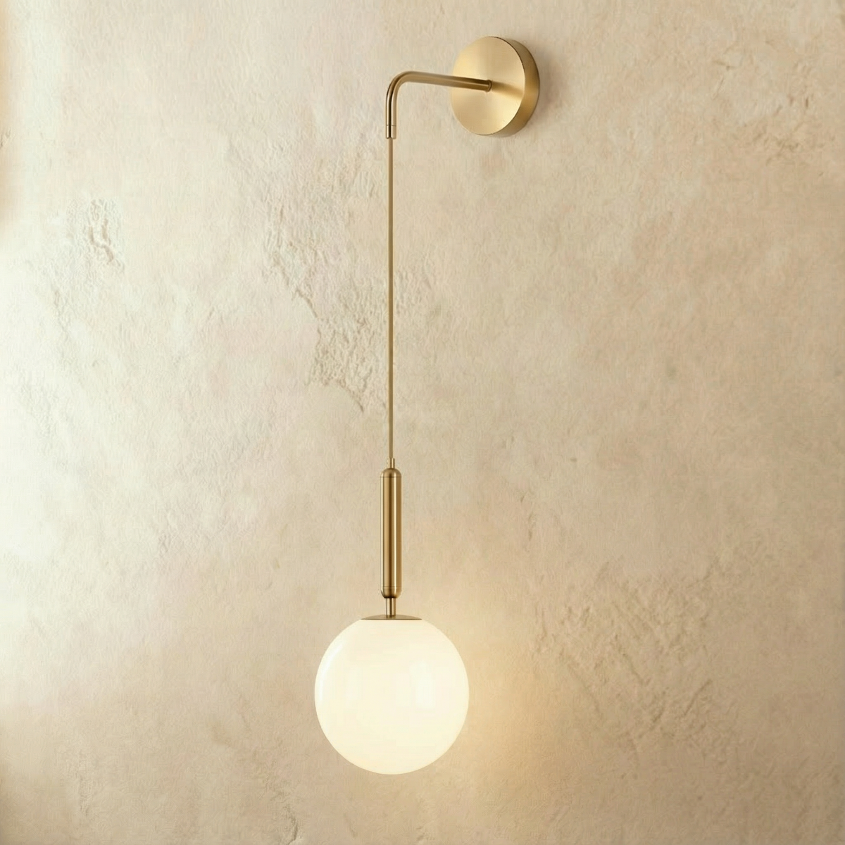Clérachic gold globe wall sconce with an angled brass arm and adjustable cable, mounted on a plain plaster wall.