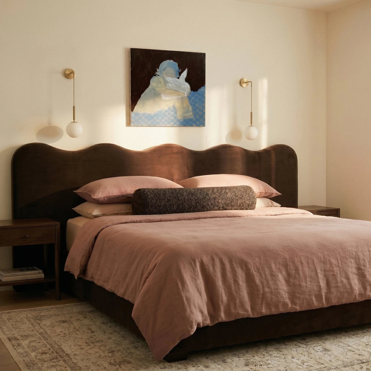Two Clérachic gold globe wall sconces flank framed art above a scalloped headboard in a warm-toned bedroom.