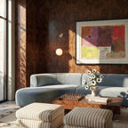 Clérachic gold globe wall sconce mounted on dark burl wood paneling beside a sofa and framed abstract artwork.