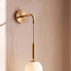 Close-up of the Clérachic gold globe sconce's brass arm, cable and opal glass globe against a blush plaster wall.