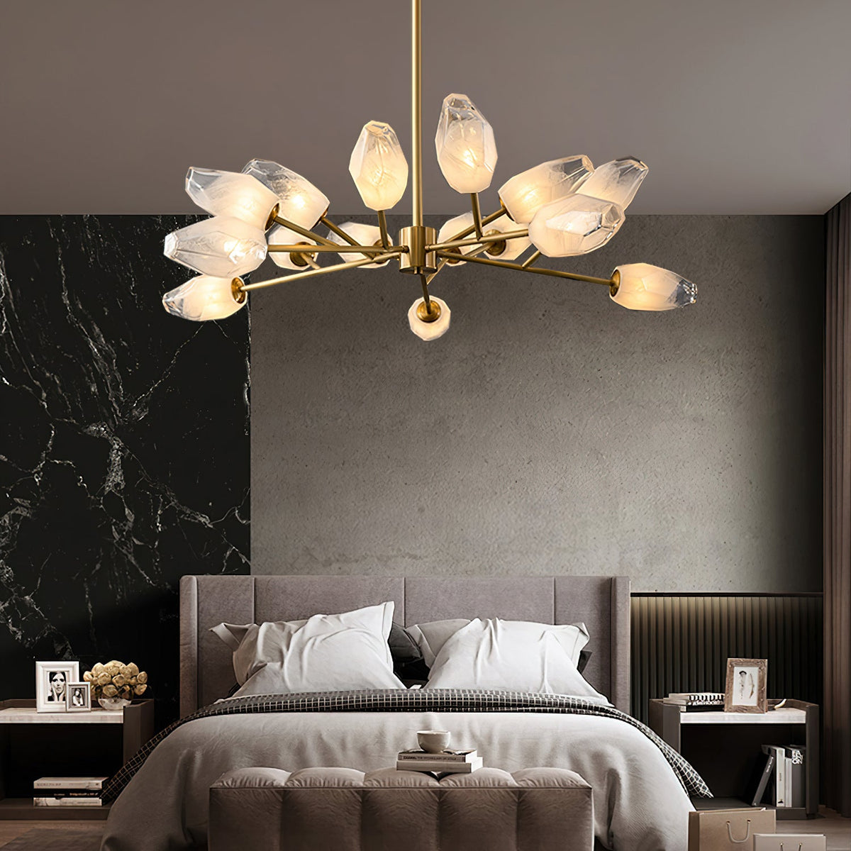 Above a made bed in a grey bedroom, a Clérachic chandelier with glowing frosted glass shades and a brass stem.