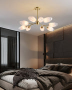 Compact Clérachic chandelier with frosted glass shades glowing in a dark, warm-toned bedroom with a rumpled throw.