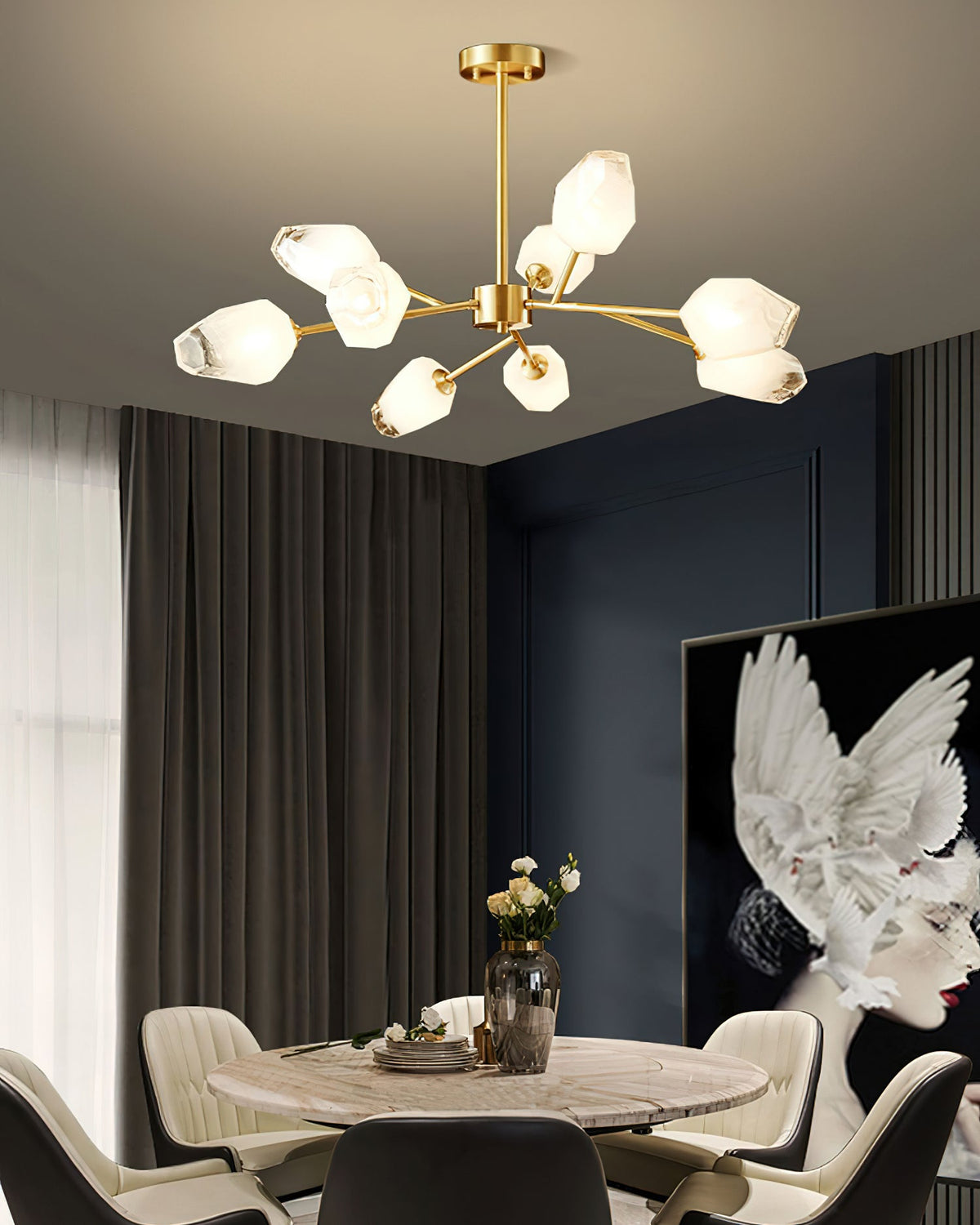 This Clérachic chandelier lit over a round dining table with cream chairs, with a dark wall panel and a vase of flowers below.
