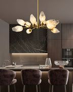 Clérachic chandelier lit above a kitchen island with plum-coloured bar stools and a dark marble splashback.