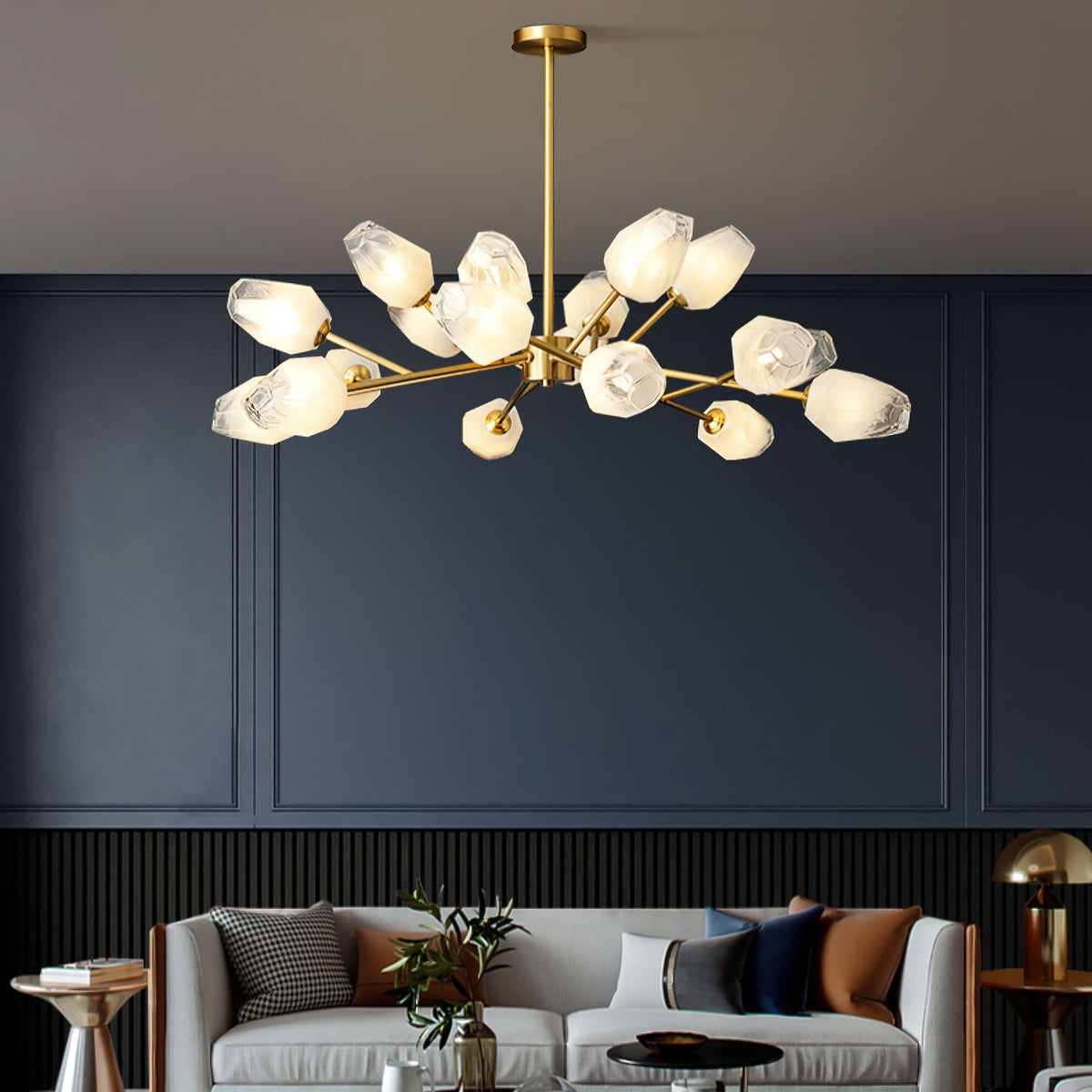 Brass chandelier with warmly lit glass shades above a grey sofa against a deep navy wall, a Clérachic light.