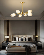 A smaller Clérachic chandelier with brass arms and frosted shades above a bed with a cream headboard and bench.