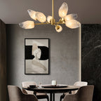 Close, low angle on a Clérachic chandelier lit above a round dining table, with a framed black and white drawing behind.