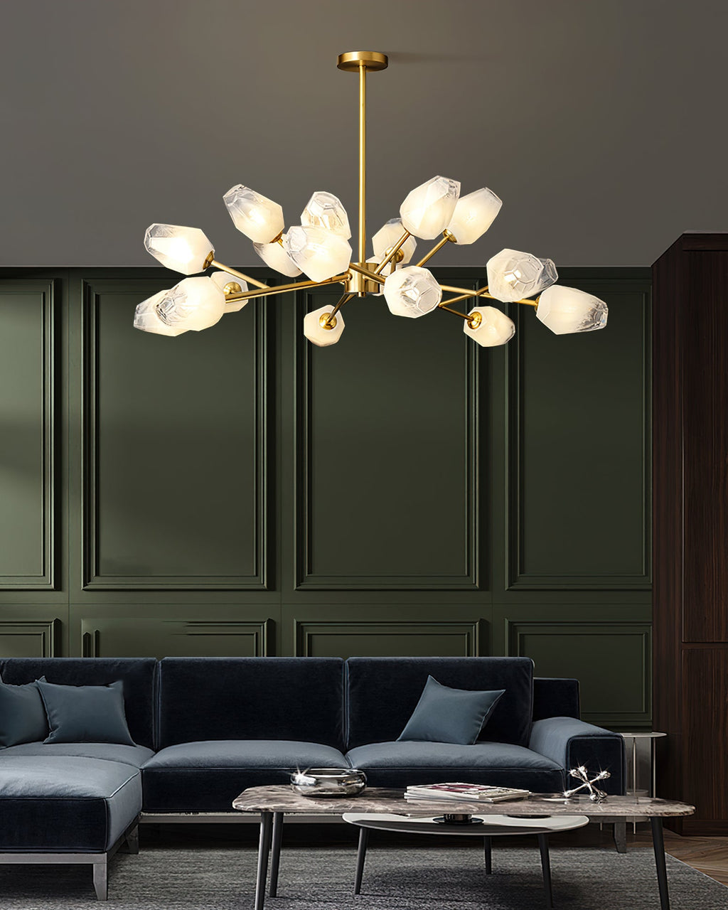 A Clérachic chandelier with frosted glass shades above a navy sofa and marble tables, set against olive-green wall panels.