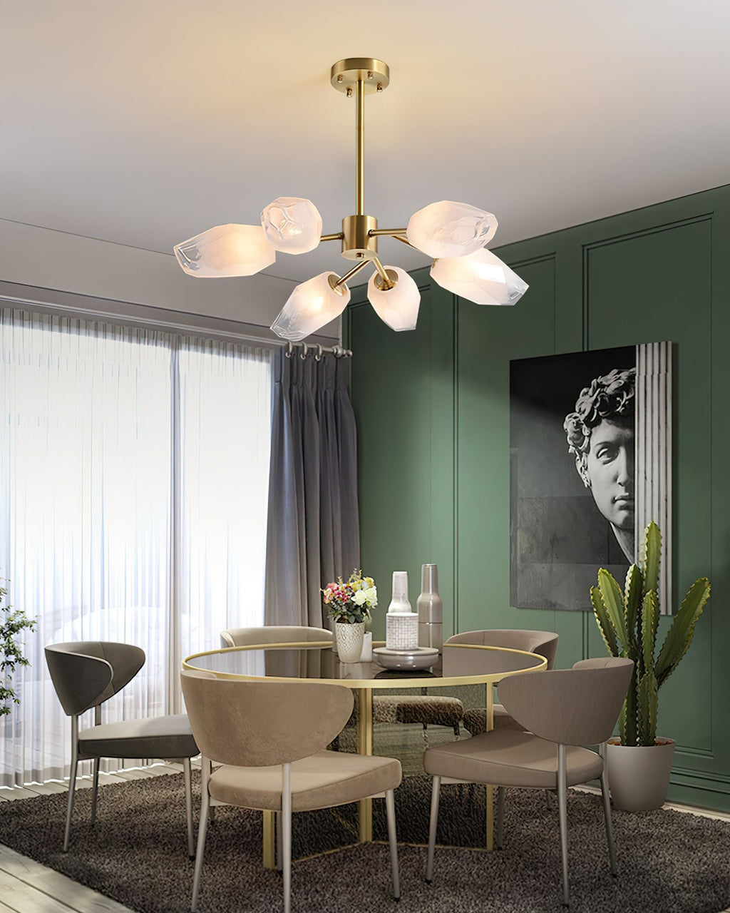 A Clérachic chandelier lit above a round glass dining table with taupe chairs, beside a green wall and sheer curtains.
