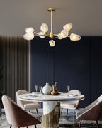 This Clérachic chandelier lit above a marble-based dining table with pink chairs and a dark navy wall behind.