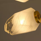 Close view of a lit, faceted frosted glass shade and brass arm end on this Clérachic chandelier.