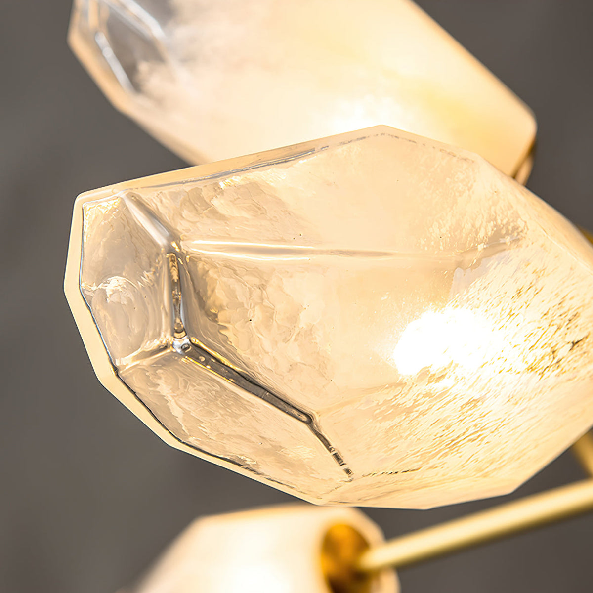 Close view of the cut, crystal-like facets on one glass shade of this Clérachic chandelier, lit from inside.