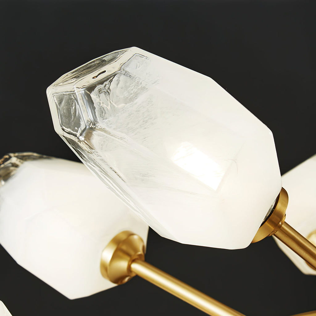 Close view of a frosted faceted glass shade and its brass arm joint on this Clérachic chandelier, on a dark backdrop.