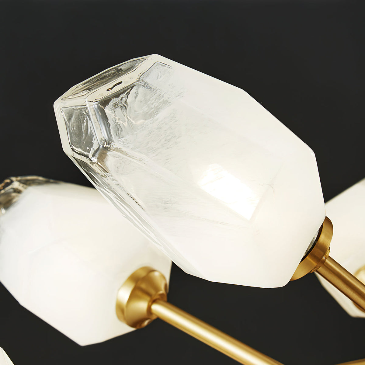 Close view of a frosted faceted glass shade and its brass arm joint on this Clérachic chandelier, on a dark backdrop.