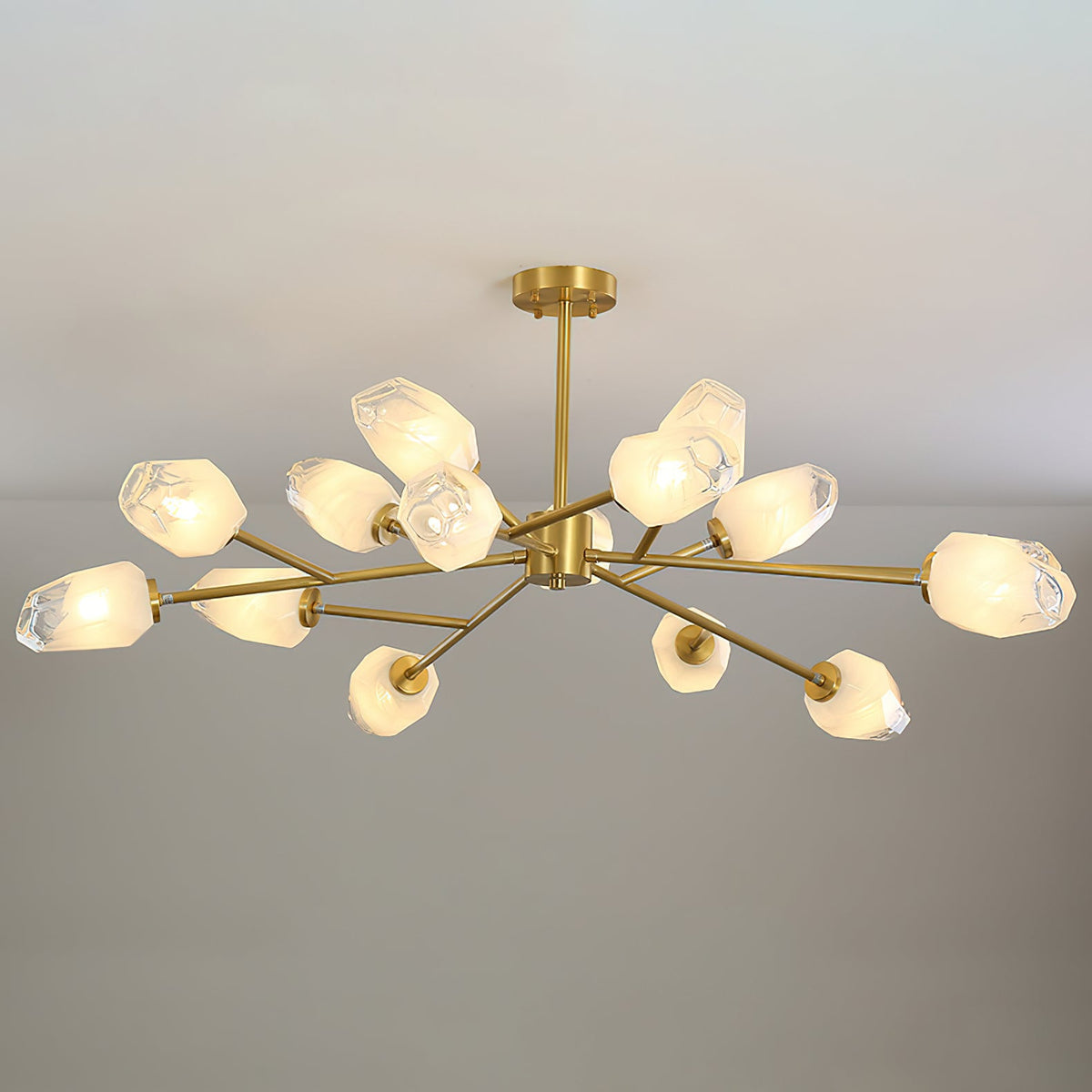 This Clérachic chandelier with a short brass stem and many shades, lit on a pale grey backdrop.