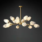 A Clérachic chandelier lit against a dark studio backdrop, with a brass rod and a wide spread of frosted shades.