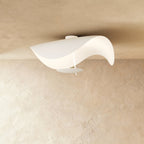 This Clérachic ceiling light in matte white curves like a wave, its round diffuser plate hanging just below the shade.