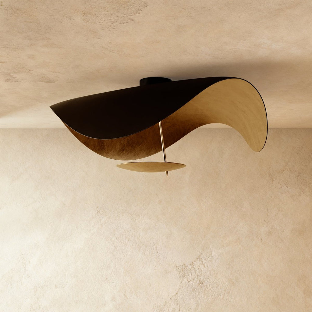 The black-and-gold Clérachic ceiling light twists into a wave form, gold leaf glowing along its inner face.