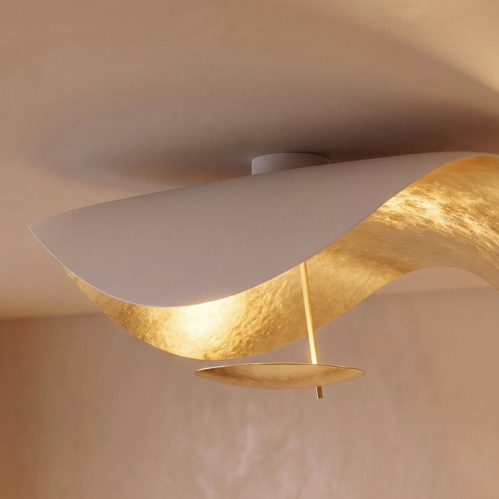 A detail shot of the Clérachic ceiling light's gold-leaf underside, its curved shell catching warm light overhead.