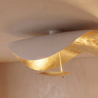 A detail shot of the Clérachic ceiling light's gold-leaf underside, its curved shell catching warm light overhead.