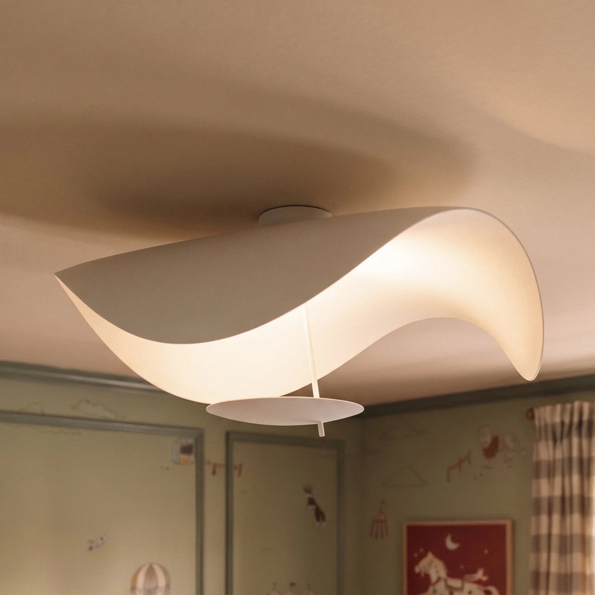 A close, illuminated view of the matte white Clérachic ceiling light, its curved form glowing warmly overhead.