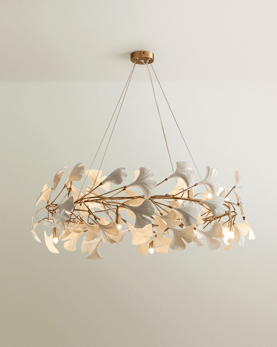 Clérachic ring chandelier of white ginkgo-style leaves on gold branches, with bare candle bulbs and a brass ceiling canopy.