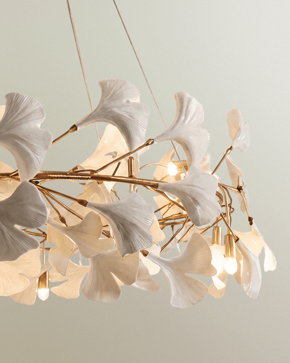 Close detail of the Clérachic chandelier showing glossy white leaves on thin gold stems and warm bare bulbs.