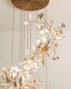 Close view of the Clérachic cascading chandelier, with white leaves on gold branches and a round brass canopy above.