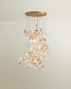 Clérachic spiralling cluster chandelier of white and gold leaves on branching stems under a round brass canopy.