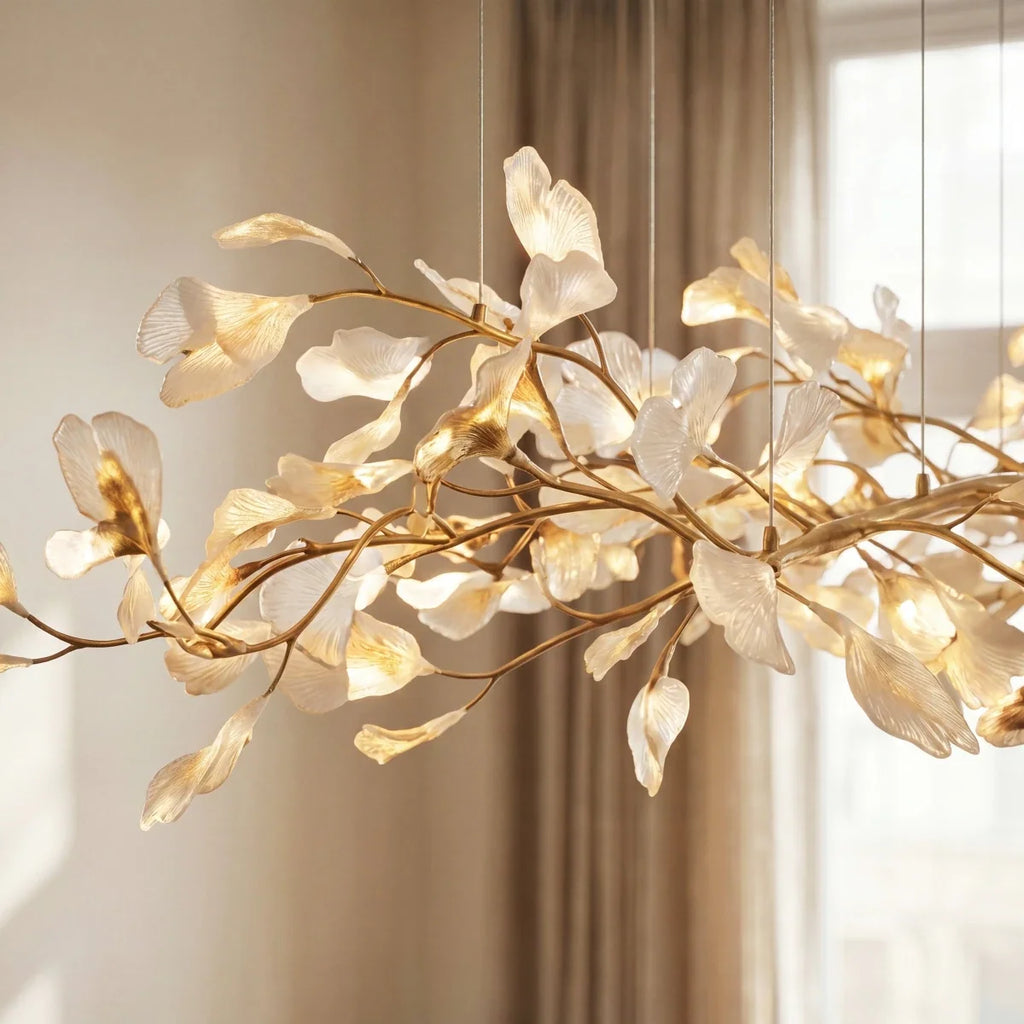 Close detail of the Clérachic linear chandelier, with translucent pale leaves on gold branches in warm window light.
