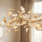 Close detail of the Clérachic linear chandelier, with translucent pale leaves on gold branches in warm window light.