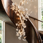Detail of the Clérachic cascade chandelier, with white leaves and small warm lights along gold branches by a wooden stair.