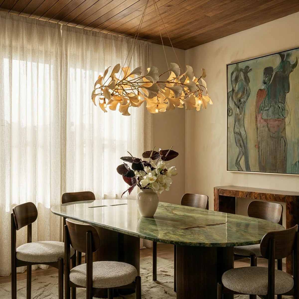 Clérachic ring chandelier of cream leaves over a green marble dining table, with a timber ceiling and sheer curtains.