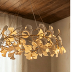 Clérachic ring chandelier of cream leaves on gold branches, with bare warm bulbs under a timber ceiling.
