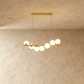 Clérachic gold linear chandelier with seven opal white glass globes along a brass bar, hung from two fine wires and a bar canopy.