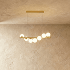 Clérachic gold linear chandelier with seven opal white glass globes along a brass bar, hung from two fine wires and a bar canopy.